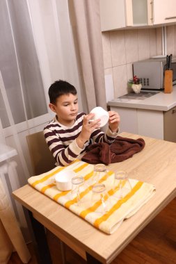 Oğlan bardakları ve bardakları havluyla siler. Ev işleri..