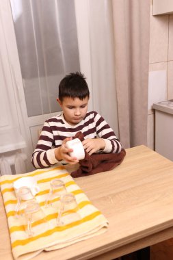 Oğlan bardakları ve bardakları havluyla siler. Ev işleri..