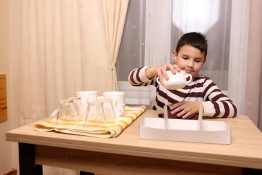 Oğlan bardakları ve bardakları havluyla siler. Ev işleri..
