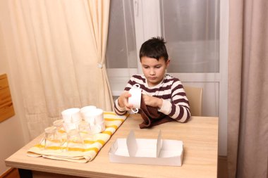 Oğlan bardakları ve bardakları havluyla siler. Ev işleri..