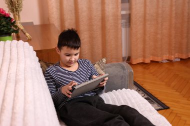 Bir çocuk kanepede otururken tablette oyun oynuyor..