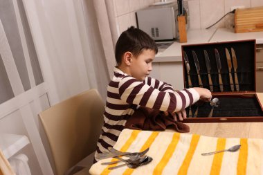 Oğlan çatal ve mutfak bıçaklarını siliyor. Ev işleri..