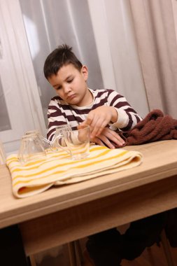 Oğlan bardakları ve bardakları havluyla siler. Ev işleri..