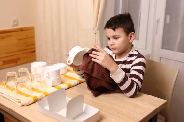 Oğlan bardakları ve bardakları havluyla siler. Ev işleri..