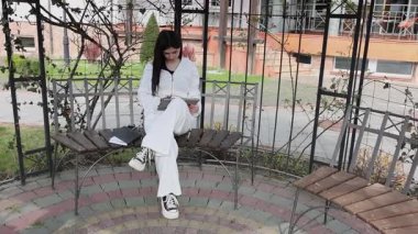 Bir kız öğrenci parkta bir bankta oturup tablet kullanarak ders çalışıyor ve notlar alıyor..