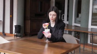 Bir kız sokakta masada otururken akıllı telefon kullanıyor ve kokteyl içiyor..