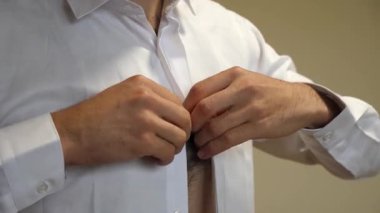 Bir adam beyaz bir gömlek giyip düğmelerini ilikliyor. Şık erkek kıyafetleri..
