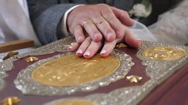 Rahip, yeni evlilerin ellerine bir haç takıyor. Birbirlerine yemin ediyorlar..