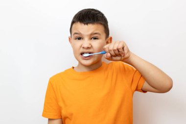 Turuncu tişörtlü küçük bir çocuk dişlerini dikkatlice fırçalıyor..