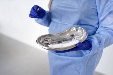 Doktor elinde cerrahi aletlerle bir tepsi tutuyor..