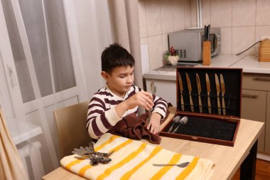 Oğlan çatal ve mutfak bıçaklarını siliyor. Ev işleri..