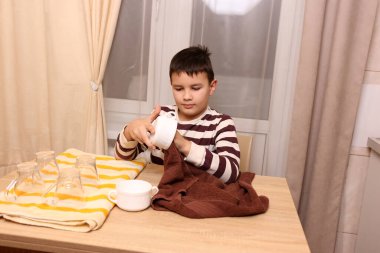 Oğlan bardakları ve bardakları havluyla siler. Ev işleri..