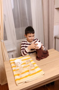 Oğlan bardakları ve bardakları havluyla siler. Ev işleri..