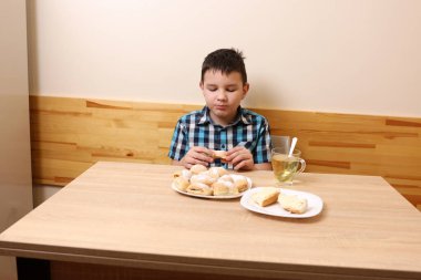 Bir çocuk masada otururken tatlı çörekler yer ve çay içer..