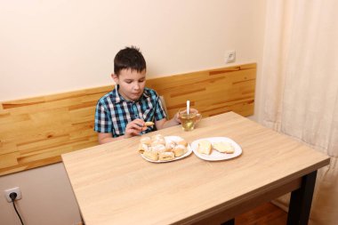 Bir çocuk masada otururken tatlı çörekler yer ve çay içer..