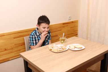 Bir çocuk masada otururken tatlı çörekler yer ve çay içer..