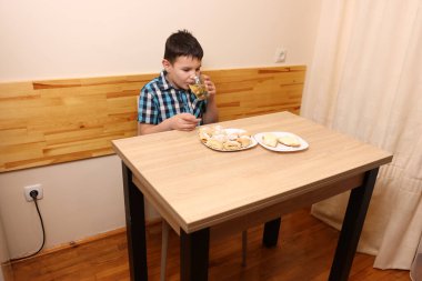 Bir çocuk masada otururken tatlı çörekler yer ve çay içer..