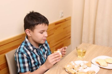 Bir çocuk masada otururken tatlı çörekler yer ve çay içer..