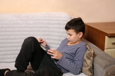 Bir çocuk kanepede otururken tablette oyun oynuyor..
