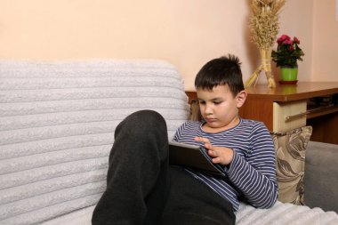 Bir çocuk kanepede otururken tablette oyun oynuyor..