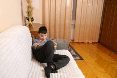 Bir çocuk kanepede otururken tablette oyun oynuyor..