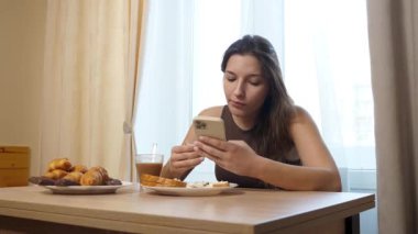 Akıllı telefon kullanırken çörek yiyip kahve içen bir kız..