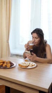 Akıllı telefon kullanırken çörek yiyip kahve içen bir kız..