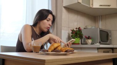 Akıllı telefon kullanırken çörek yiyip kahve içen bir kız..