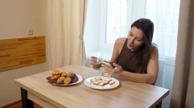Akıllı telefon kullanırken çörek yiyip kahve içen bir kız..