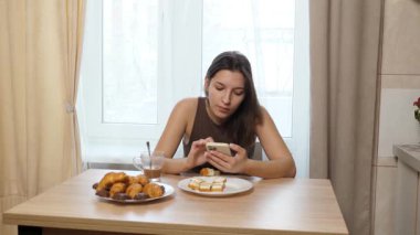 Akıllı telefon kullanırken çörek yiyip kahve içen bir kız..