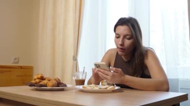 Akıllı telefon kullanırken çörek yiyip kahve içen bir kız..