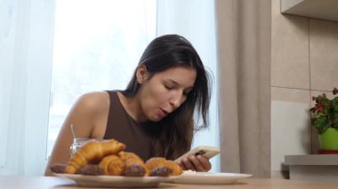 Kız kruvasan yiyor ve akıllı telefon kullanırken kahve içiyor..