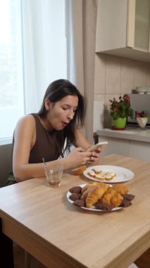 Kız kruvasan yiyor ve akıllı telefon kullanırken kahve içiyor..