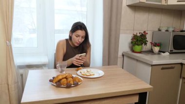 Kız kruvasan yiyor ve akıllı telefon kullanırken kahve içiyor..