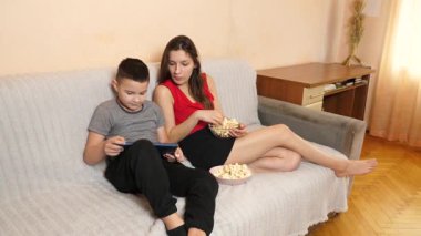 Erkek ve kız kardeş tablette oyun oynayıp patlamış mısır yiyorlar..