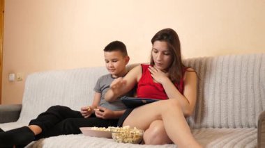 Erkek ve kız kardeş tablette oyun oynayıp patlamış mısır yiyorlar..