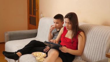 Erkek ve kız kardeş tablette oyun oynayıp patlamış mısır yiyorlar..