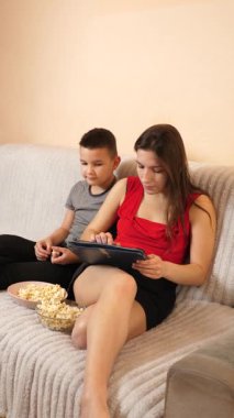 Erkek ve kız kardeş tablette oyun oynayıp patlamış mısır yiyorlar..