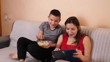 Erkek ve kız kardeş tablette oyun oynayıp patlamış mısır yiyorlar..