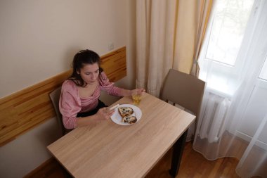 Bir kız çörekle çay içiyor ve akıllı telefon kullanıyor..