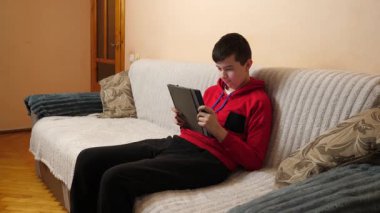 Bir genç kanepede otururken tablet kullanır..