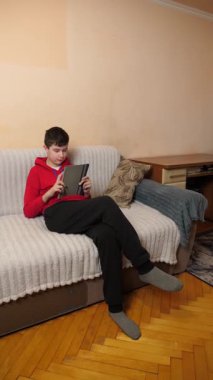 Bir genç kanepede otururken tablet kullanır..