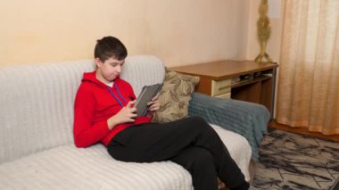 Bir genç kanepede otururken tablet kullanır..