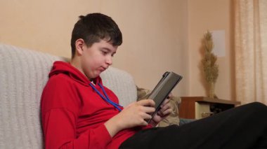 Bir genç kanepede otururken tablet kullanır..