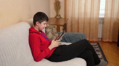 Bir genç kanepede otururken tablet kullanır..