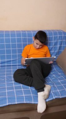 Bir çocuk kanepede otururken tahta üzerine bir kalemle resim çizer..