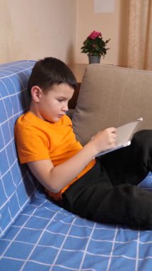 Bir çocuk kanepede otururken tahta üzerine bir kalemle resim çizer..