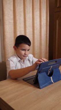 Bir çocuk masada otururken tablette oyunlar oynuyor..