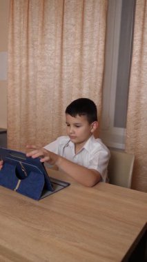 Bir çocuk masada otururken tablette oyunlar oynuyor..