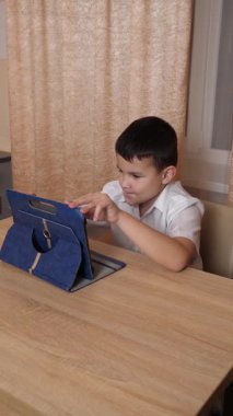 Bir çocuk masada otururken tablette oyunlar oynuyor..